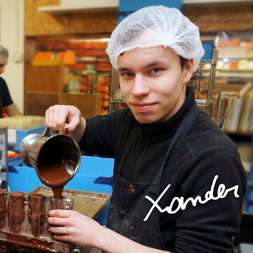 Jonge man met haarnetje giet chocolade in vormen in een bakkerij.